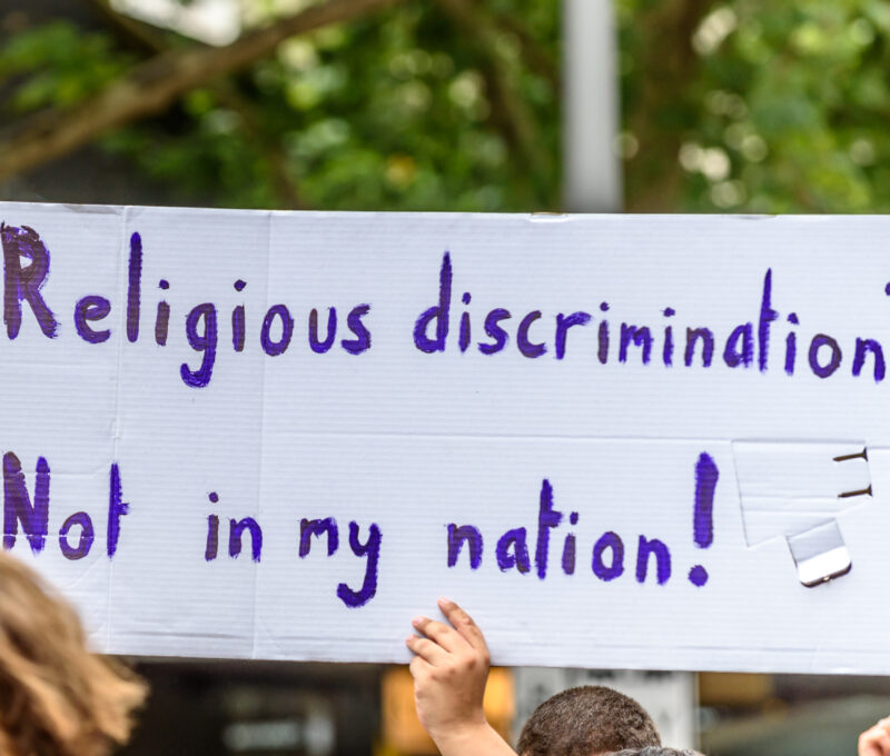person holding a sign reading "religious discrimination? not in my nation!"